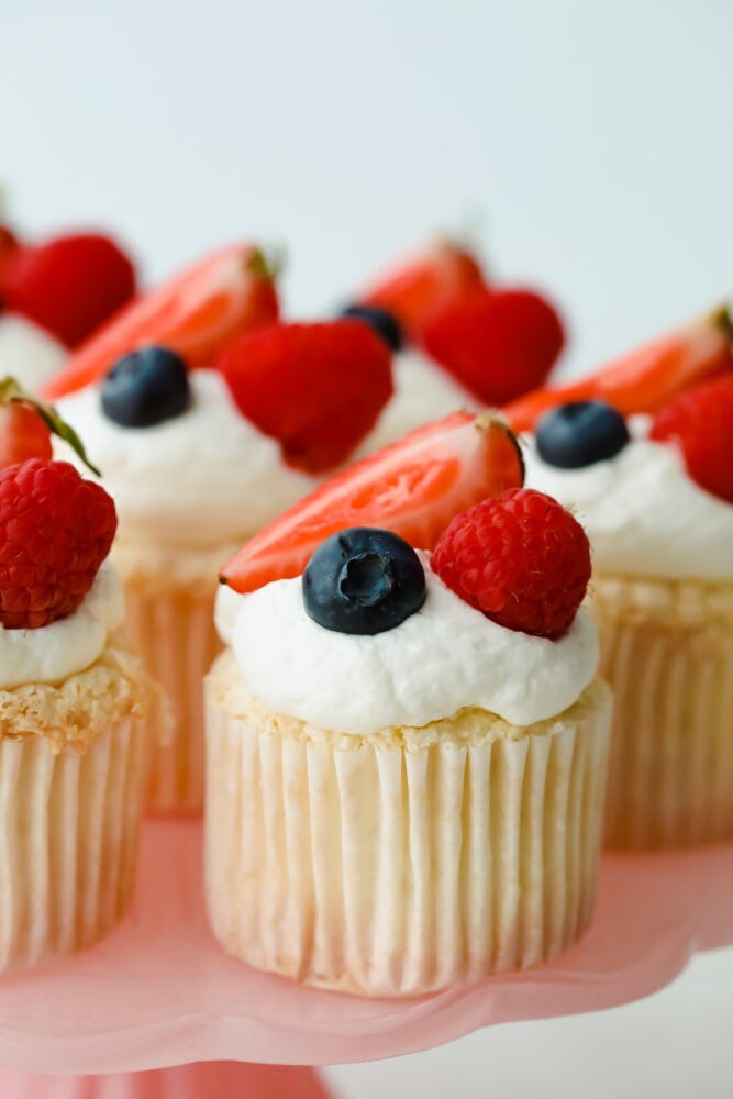 These ultra-fluffy, delicate cupcakes are the best base for light and tasty summer treats. Top with fresh whipped cream frosting and berries for a dessert that is a perfect combination of airy and sweet. Angel Food Cupcakes on serving dish.