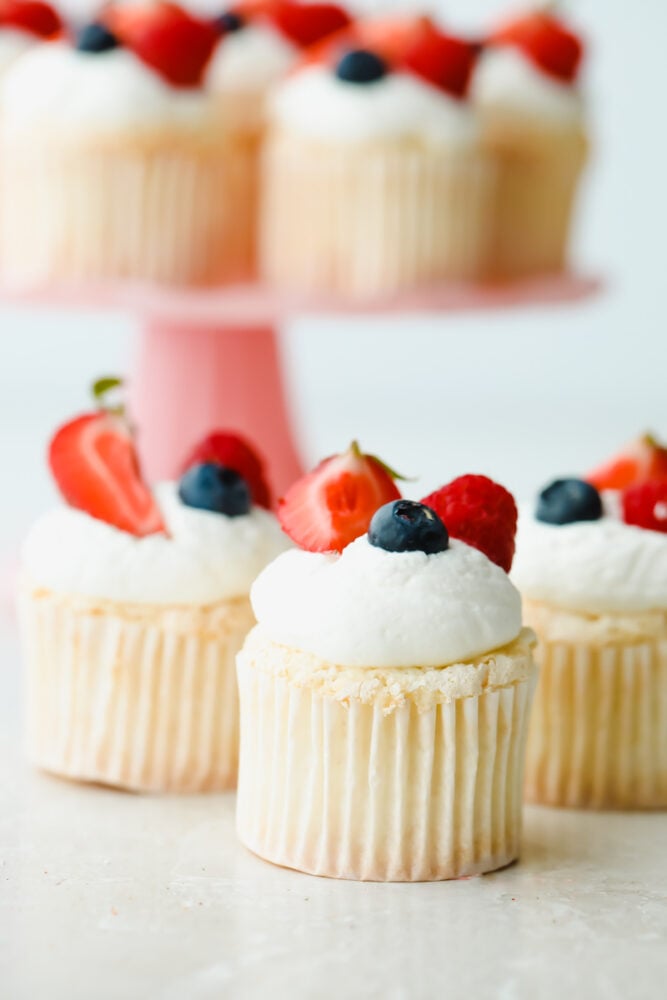 These ultra-fluffy, delicate cupcakes are the best base for light and tasty summer treats. Top with fresh whipped cream frosting and berries for a dessert that is a perfect combination of airy and sweet. Angel Food Cupcakes topped with blueberries and strawberries.