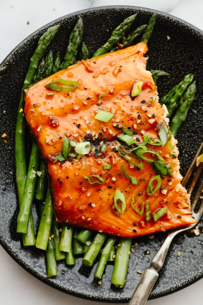 Blanketed with an insanely good soy garlic glaze, this juicy Asian glazed salmon is to die for! With how healthy and delicious it is, it will become your new lunch go-to! Asian glazed salmon served on top of asparagus.