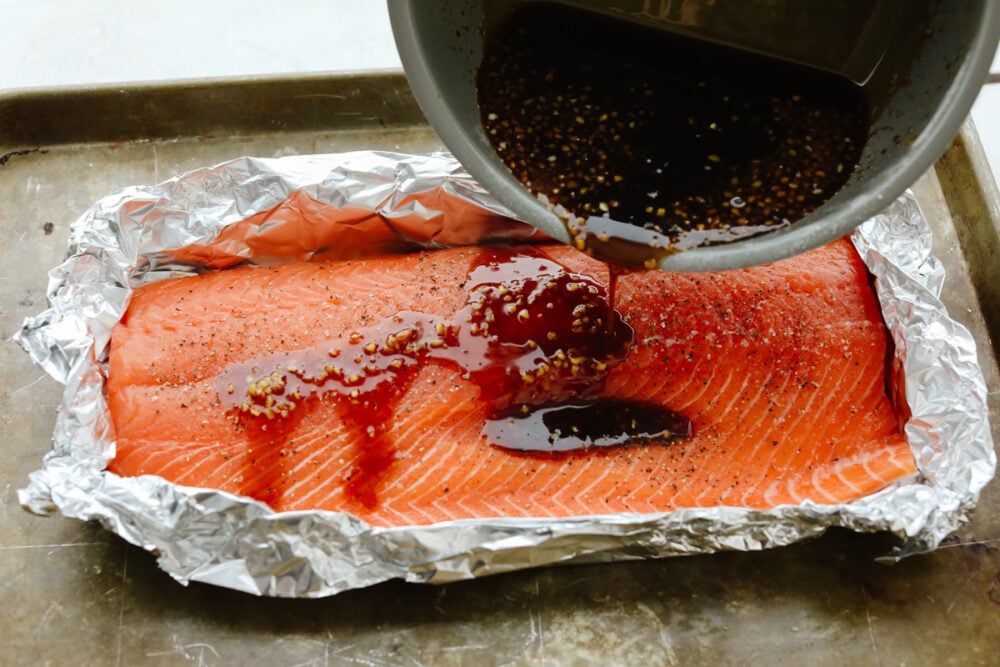 Blanketed with an insanely good soy garlic glaze, this juicy Asian glazed salmon is to die for! With how healthy and delicious it is, it will become your new lunch go-to! Pouring glaze over salmon in tin foil.