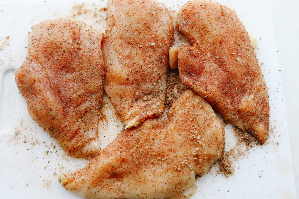 This perfect and juicy baked chicken will be sure to get a WOW at your next family get-together! It is seasoned with a delightful array of spices and baked to perfection! Your tastebuds will thank you later!! Raw chicken with a rub of spices on it.
