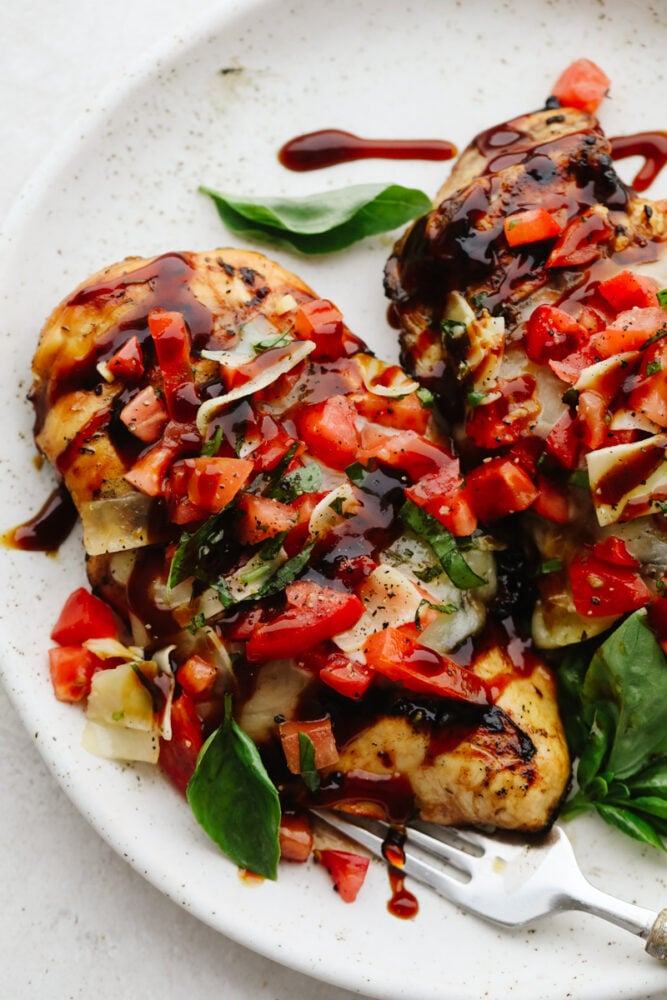 Bruschetta chicken is a delicious, low-carb meal that packs big, mouthwatering flavor. With fresh vegetables, garlic, a sticky-sweet balsamic glaze, and homemade Italian Seasoning, this will be your new go-to lunch. Bruschetta chicken on a white plate.