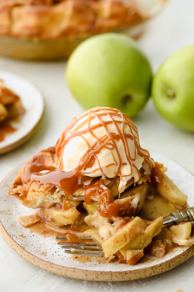 Caramel Apple Pie is the traditional American dessert, but totally elevated. Sour tart apples are smothered in caramel, it's insanely delicious. A slice of caramel apple pie with ice cream and caramel drizzled on top.