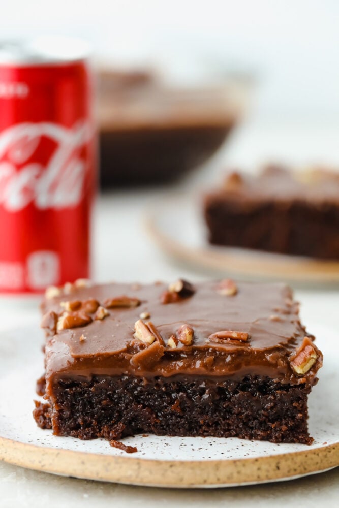 Coca Cola cake is an easy-to-make chocolate cake, topped with pecans and ooey-gooey chocolate frosting. It is so easy and absolutely delicious, you are going to love this cake and its subtle soda flavor! A slice of Coca-Cola cake topped with nuts.