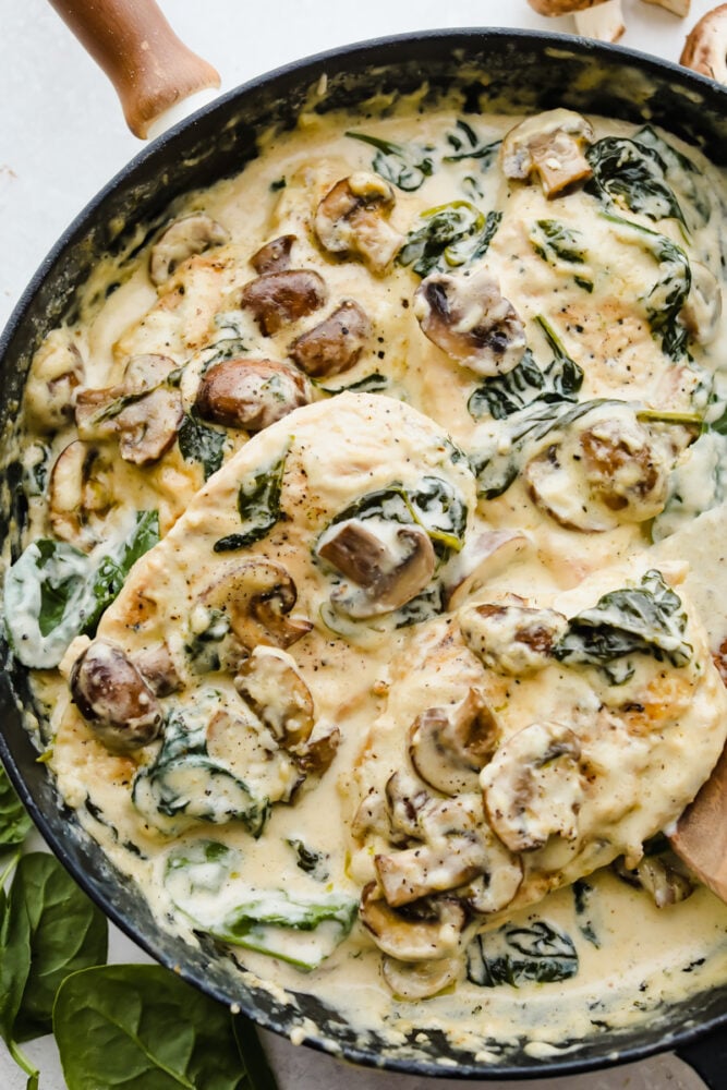 Creamy Parmesan Garlic Mushroom Chicken is ready in just 30 minutes and the parmesan garlic sauce will wow the entire family! This will become a new favorite! Scooping the chicken in the pan with the sauce and mushrooms and spinach.
