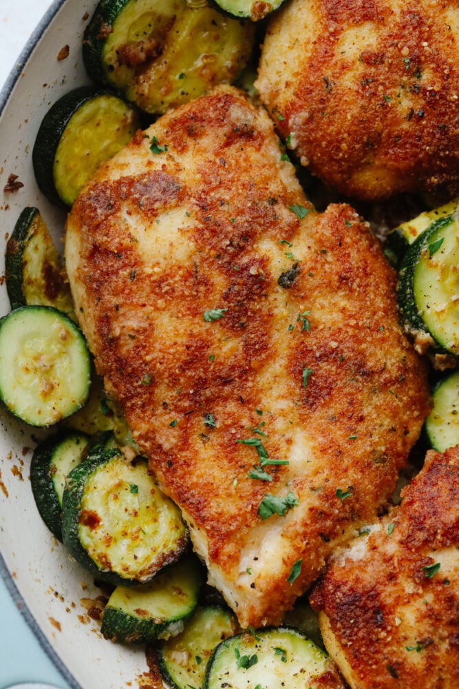 Crispy parmesan garlic chicken with zucchini is a fantastic one-pan meal that the family will love. Crispy chicken is breaded with an amazing parmesan garlic crust paired with tender zucchini sautรฉed to perfection! Close-up of crispy parmesan garlic chicken and zucchini.