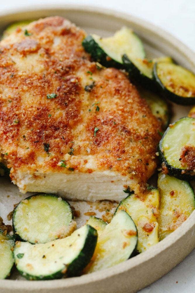 Crispy parmesan garlic chicken with zucchini is a fantastic one-pan meal that the family will love. Crispy chicken is breaded with an amazing parmesan garlic crust paired with tender zucchini sautรฉed to perfection! Slice cut out of parmesan garlic chicken with zucchini.