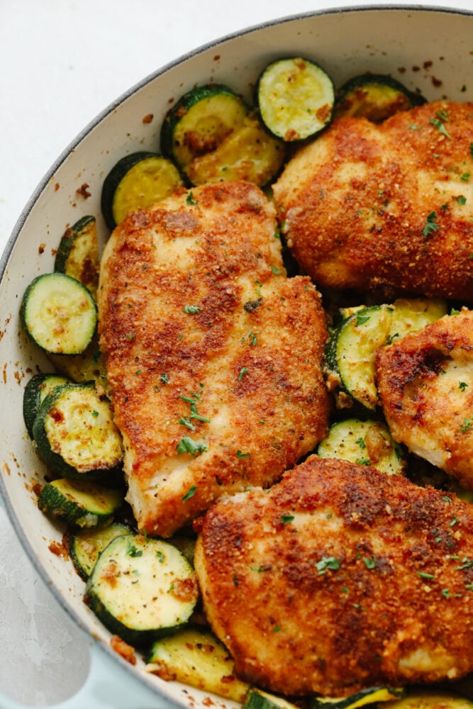 Crispy parmesan garlic chicken with zucchini is a fantastic one-pan meal that the family will love. Crispy chicken is breaded with an amazing parmesan garlic crust paired with tender zucchini sautรฉed to perfection! Cooked parmesan garlic chicken and zucchini in a white bowl.