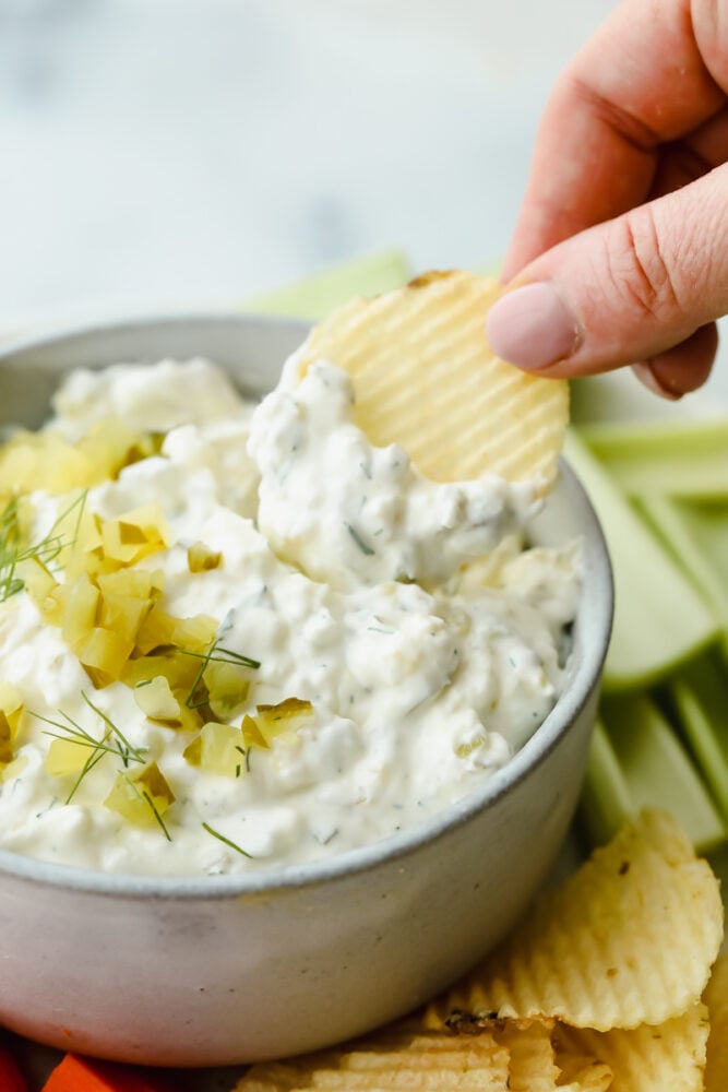 Calling all pickle lovers! Loaded with chopped pickles and herbs, dill pickle dip is bursting with flavor and absolutely irresistible! Putting dill pickle dip on a potato chip.