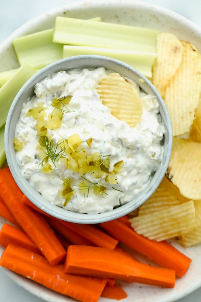 Calling all pickle lovers! Loaded with chopped pickles and herbs, dill pickle dip is bursting with flavor and absolutely irresistible! Dill pickle dip on serving dish with chips and veggies.