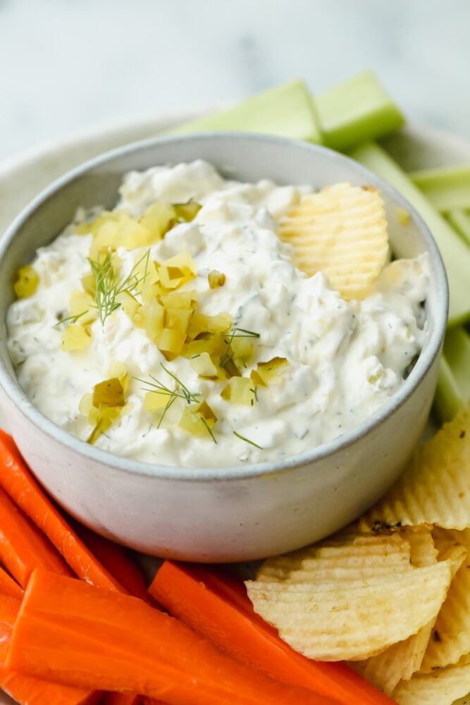 Calling all pickle lovers! Loaded with chopped pickles and herbs, dill pickle dip is bursting with flavor and absolutely irresistible! Dill pickle dip with potato chips, celery, and carrots.