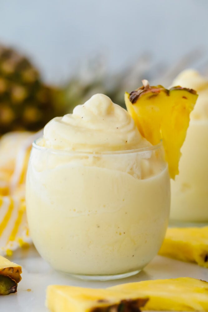Dole Pineapple Whips are the perfect summertime treat that you can make at home. Similar to Disneyland's and Hawaii's Dole whips, they are refreshing and quick. Dole pineapple whip in a glass with fresh pineapple garnish.
