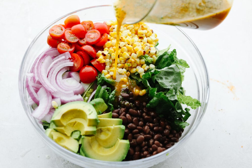 This easy grilled shrimp salad recipe is the perfect solution to your summer dinner needs! Itโs healthy, quick, and full of grilled chipotle flavor. Pouring chipotle dressing over vegetbles.