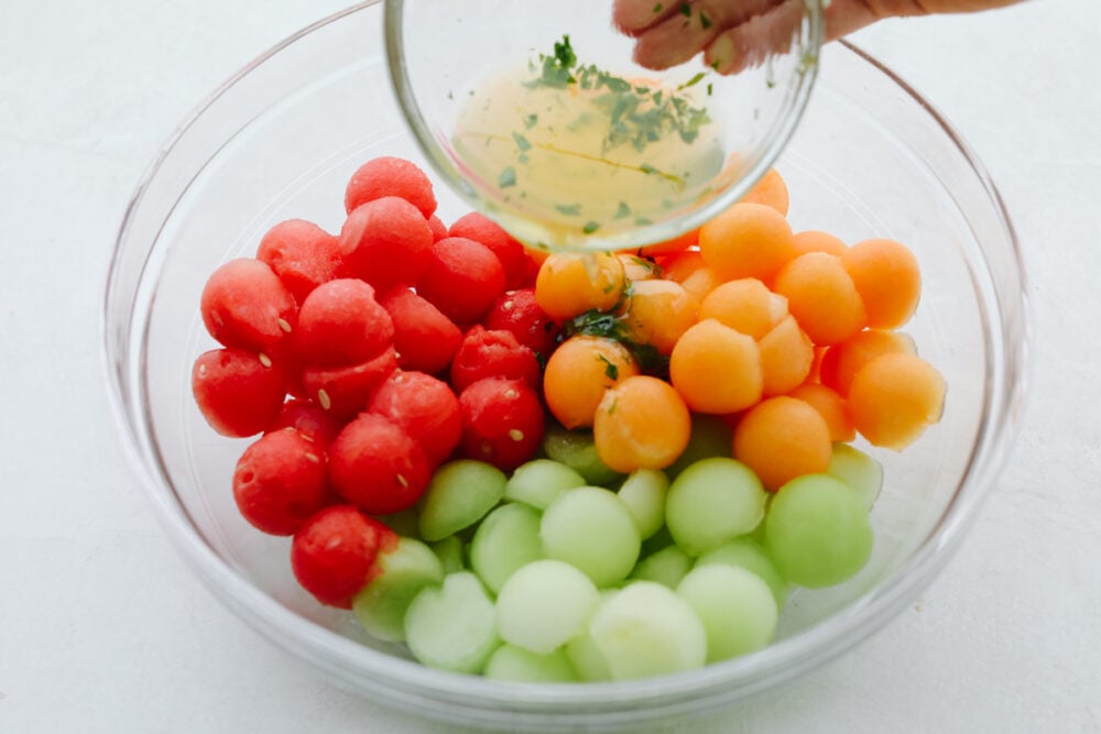 I don't know about you but nothing hits the spot more on a hot summer day than fresh fruit and salads! Combine the two together and our melon salad will leave you feeling refreshed and satisfied! A bowl filled with watermelon, honeydew and cantaloupe scooped in small sizes with dressing being poured on them.