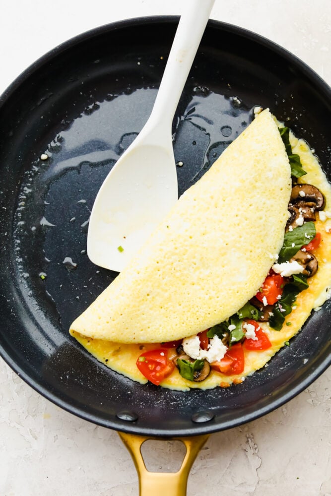 Savory breakfast omelets are so classic and my go to for a home run breakfast! Quick, easy, and delicious, this healthy breakfast option will leave you feeling full and satisfied! An omelet in a pan, filled with ingredients being folded in half.