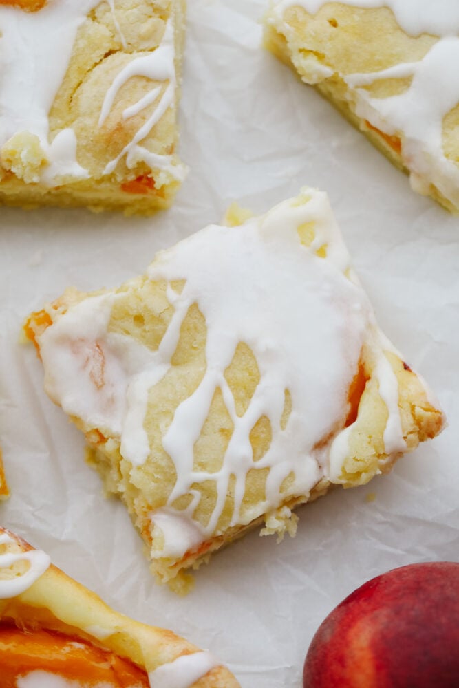 Delicious bars that have a creamy cheesecake and peach pie filling in the center. They are drizzled in a glaze and taste just like you are biting into a peach pie! Peaches and cream pie bars cut into squares.