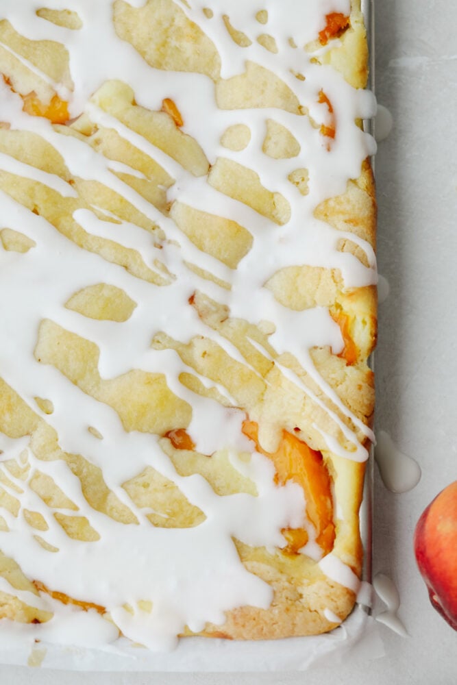 Peaches and Cream Pie Bars are delicious bars that have a creamy cheesecake and peach pie filling in the center. They are drizzled in a glaze and taste just like you are biting into a peach pie! An overview photo of the peaches and cream pie bars in a sheet pan.