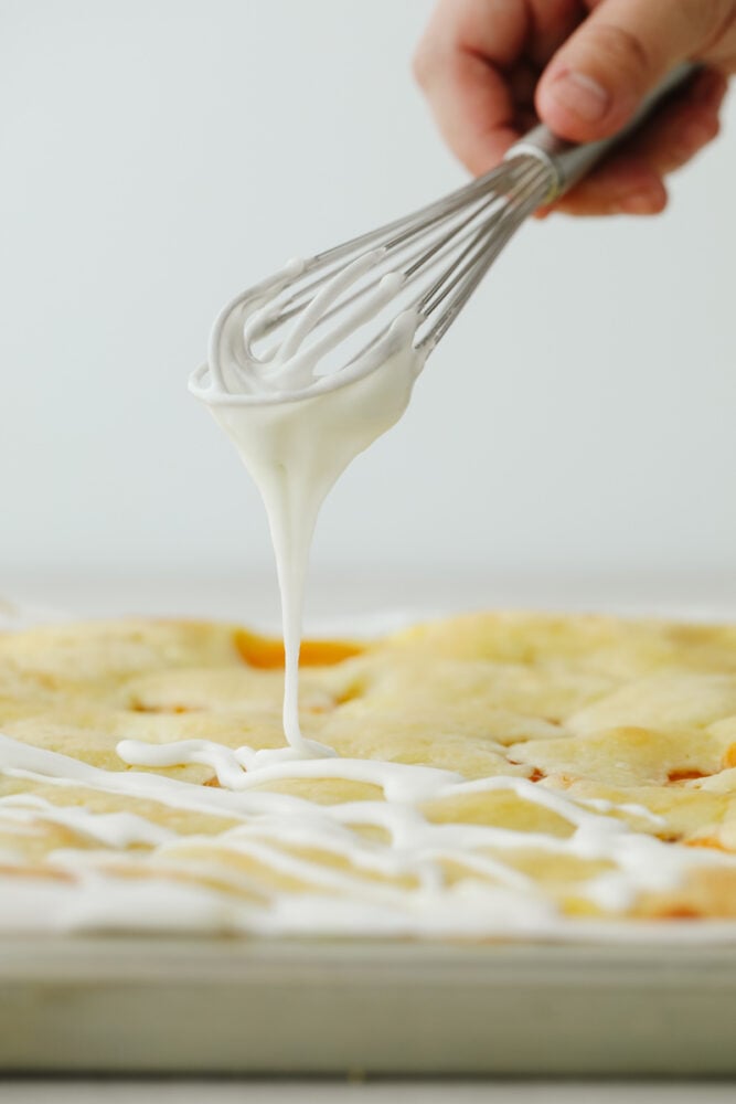 Peaches and Cream Pie Bars are delicious bars that have a creamy cheesecake and peach pie filling in the center. They are drizzled in a glaze and taste just like you are biting into a peach pie! Frosting the tops of the peaches and pie bars.