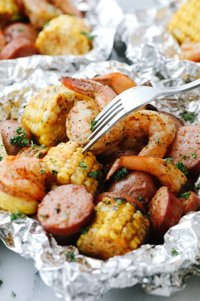 Shrimp Boil Foil Packets bring you juicy, tender shrimp and veggies tossed in Cajun spices! These pack all the kick and amazing flavor of Cajun cooking without the mess! Taking a bite of corn in a Shrimp Boil Foil Packet.
