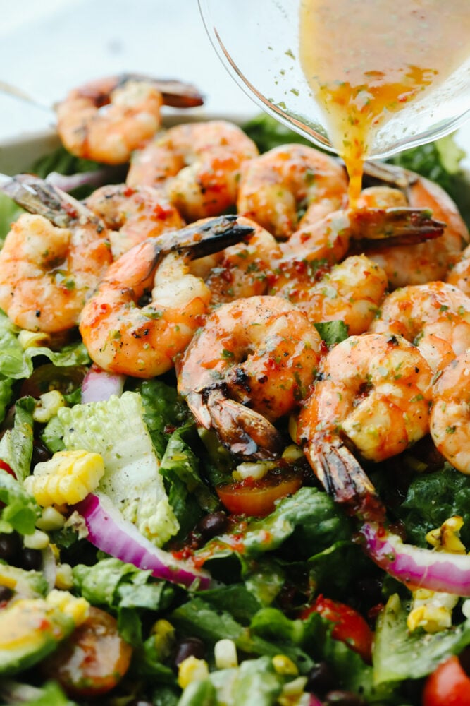 This easy grilled shrimp salad recipe is the perfect solution to your summer dinner needs! Itโs healthy, quick, and full of grilled chipotle flavor. Pouring dressing over greens and grilled shrimp.