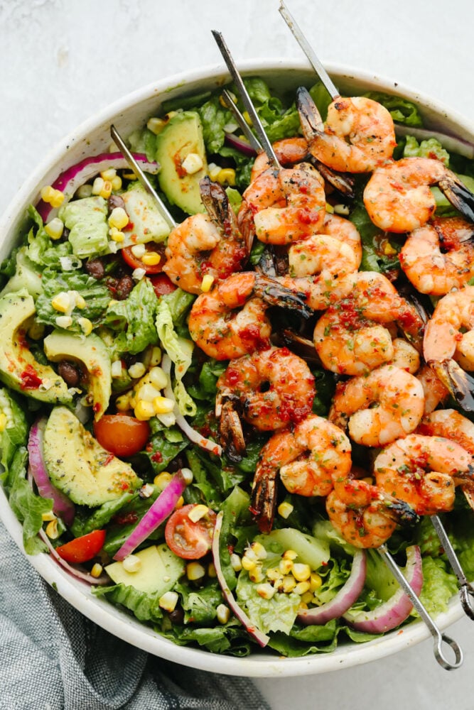 This easy grilled shrimp salad recipe is the perfect solution to your summer dinner needs! Itโs healthy, quick, and full of grilled chipotle flavor. Greens in a white bowl topped with grilled shrimp.