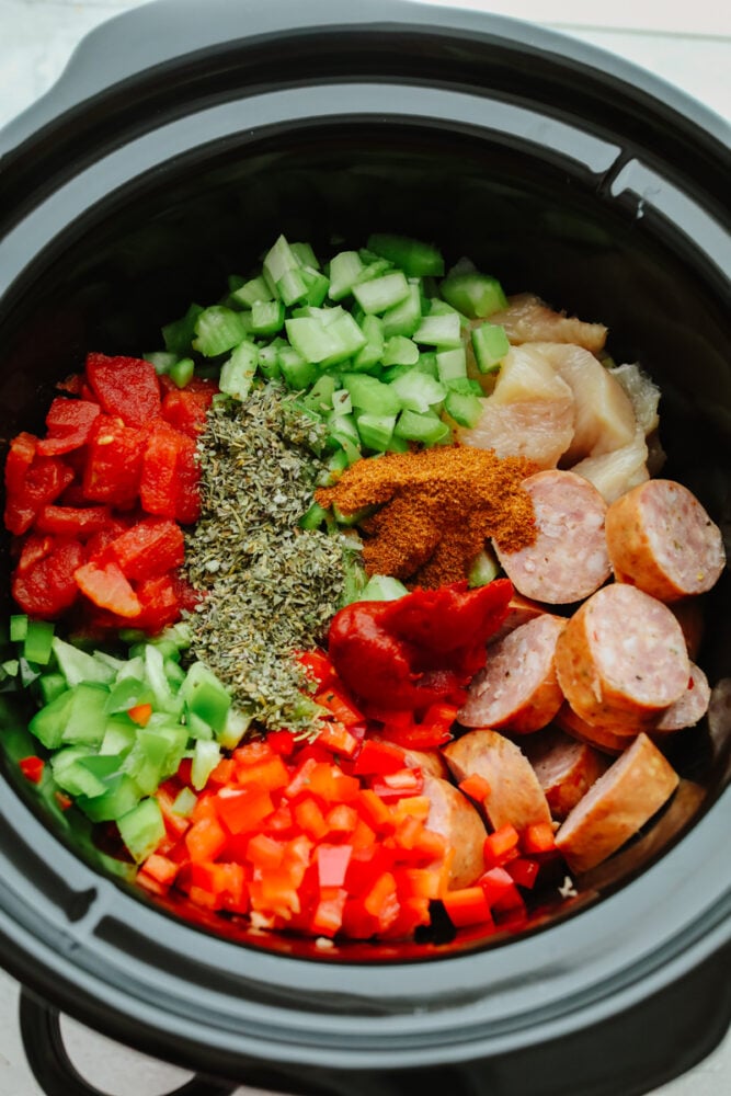 Slow Cooker Jambalaya is loaded with tasty sausage, chicken, and shrimp that gets cooked low and slow to activate the bold spices. This hearty dinner is an effortless meal that is ready with only 10 minutes of prep! Vegetables, spices, chicken, and sausage in a slow cooker.