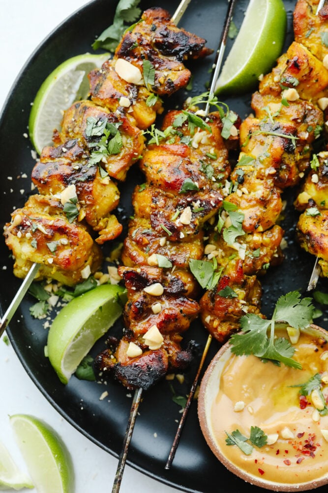 These Thai chicken skewers are marinated in coconut milk, curry and spices and then grilled to perfection. It's a quick and easy meal that's packed full of flavor! Thai Chicken skewers on a plate garnished with cilantro and peanuts.