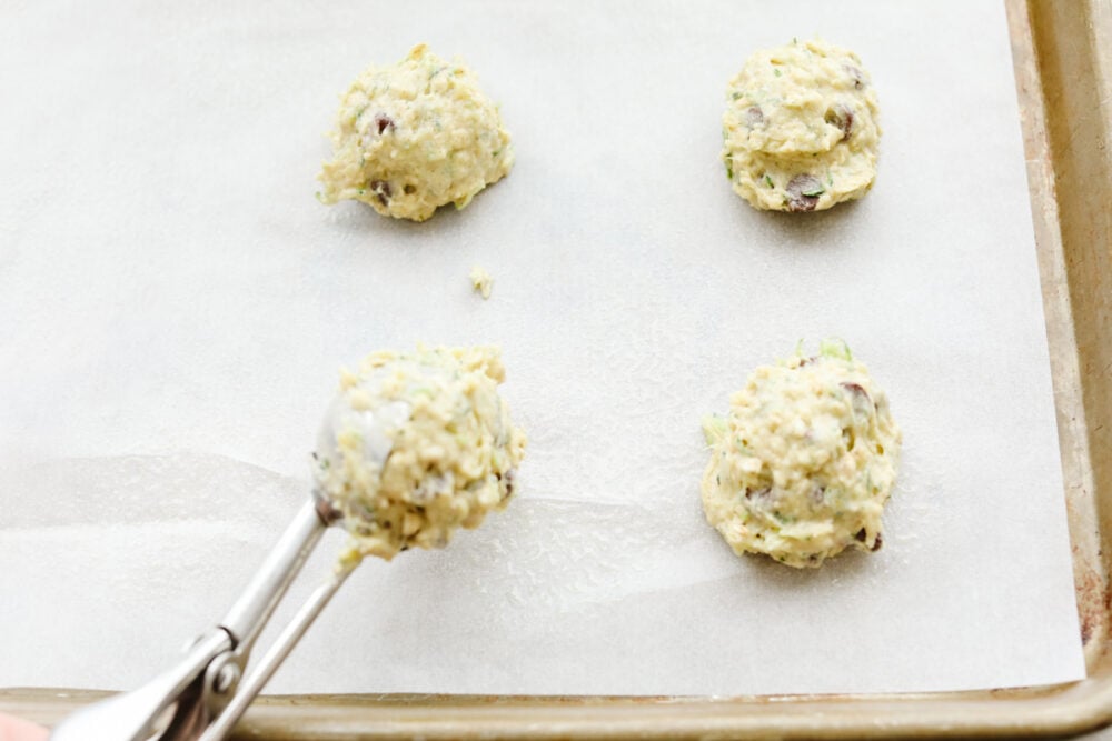 These zucchini oat chocolate chip cookies are a twist on the traditional cookie recipe and are absolutely delicious! Cookies are the ultimate comfort food that we all love and adore and after trying these, I bet you won't be able to just have one!! Scooping the dough onto parchment paper.