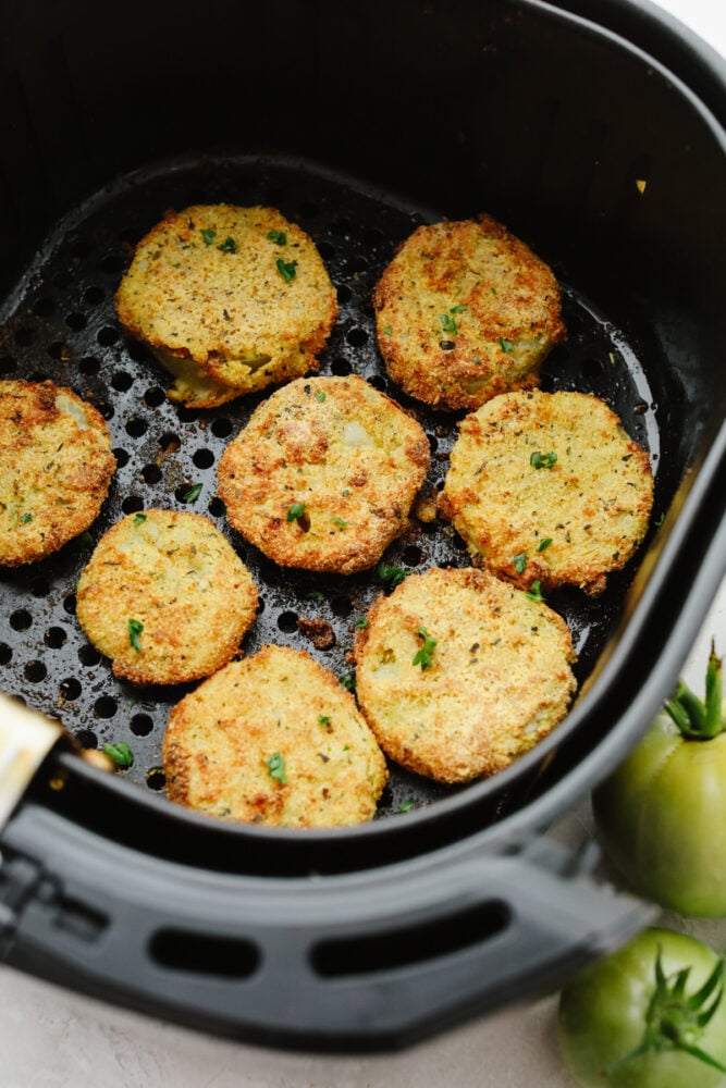 Air fryer fried green tomatoes are insanely delicious! Crispy on the outside and tender and juicy on the inside, these tomatoes will knock your socks off! Green tomatoes frying in an air fryer.