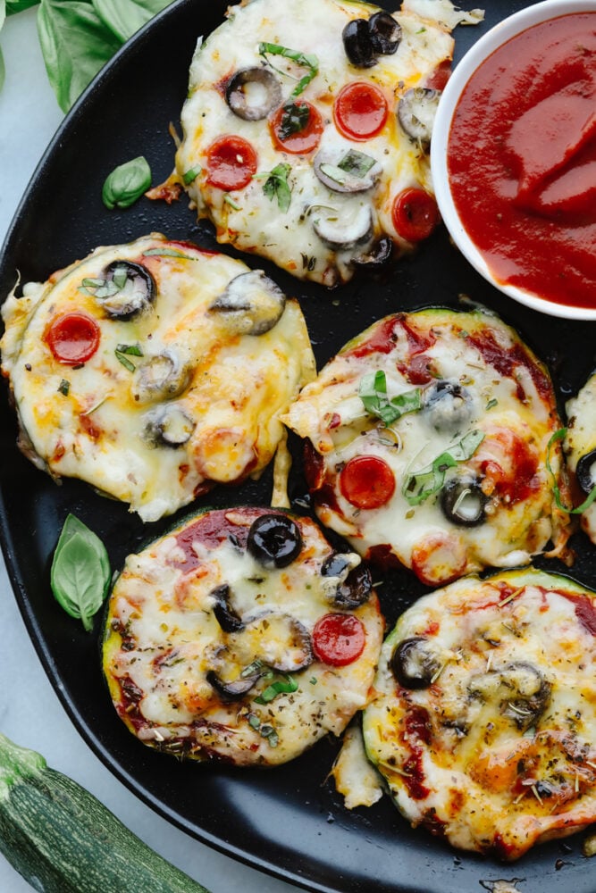Air Fryer Zucchini Pizza Bites are the perfect low-carb way to eat your pizza and love it too! Quick and easy these make a perfect snack, appetizer, or light meal any time of the week! Pizza bites on a plate with a side of marinara.