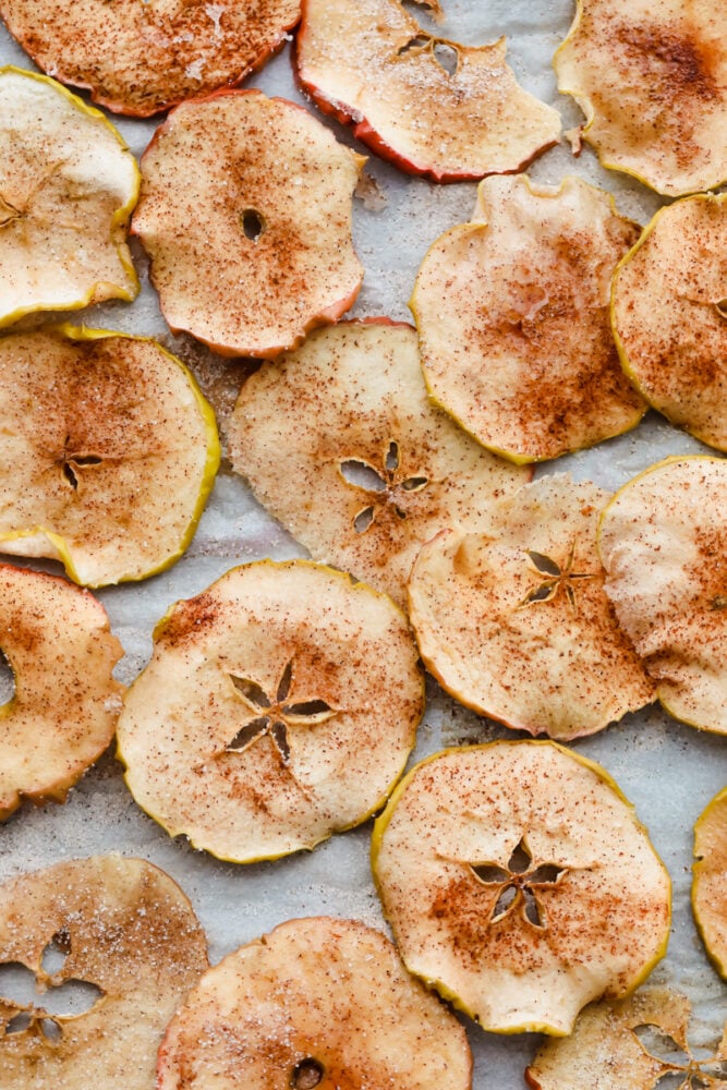 Baked Cinnamon Sugar Apple Chips is a healthy crunchy snack that is going to impress! Crunchy, crispy, sweet, and a bit spicy, these are going to change snack time Baked apple chips on parchment.