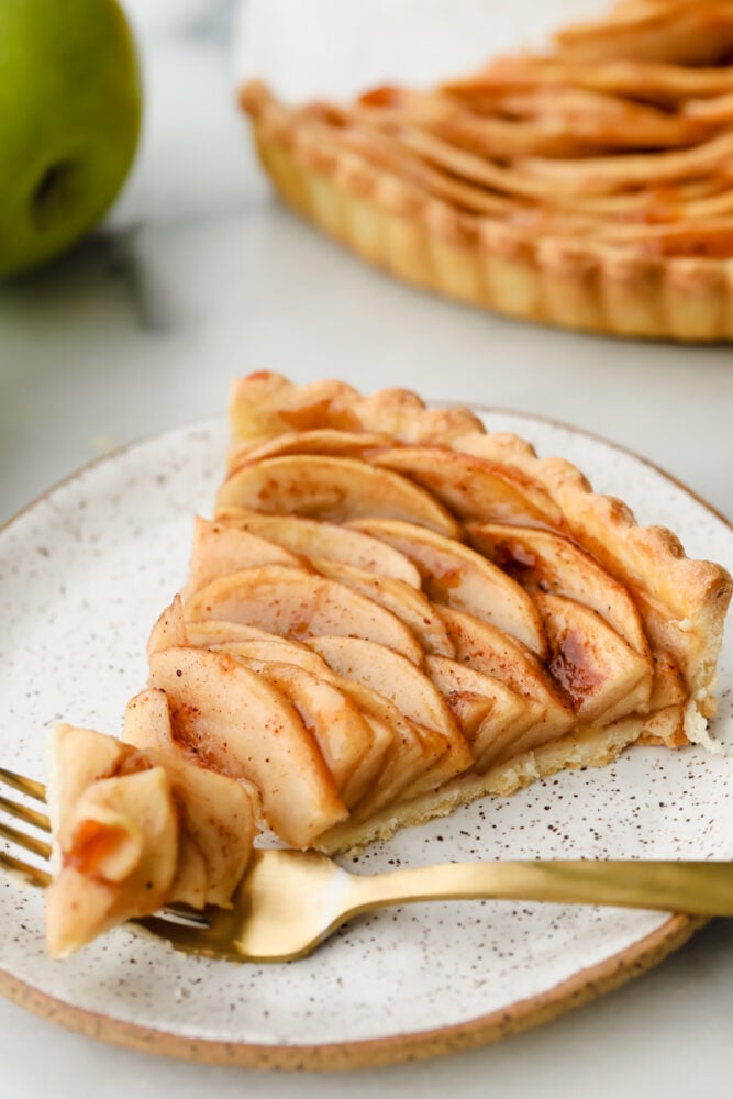 Loaded with fresh apples and baked to a perfect golden brown, this beautiful apple tart is the pastry of the summer! A combination of buttery, nutty, and tart, it tastes as good as it looks! Taking a bite of an apple tart slice.