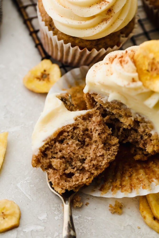 Homemade banana cupcakes that are extra fluffy and moist are the ultimate dessert! Swirled on top is a tangy cream cheese frosting that makes these so perfect, you won't be able to stop at just one! A cupcake being cut into with a fork.