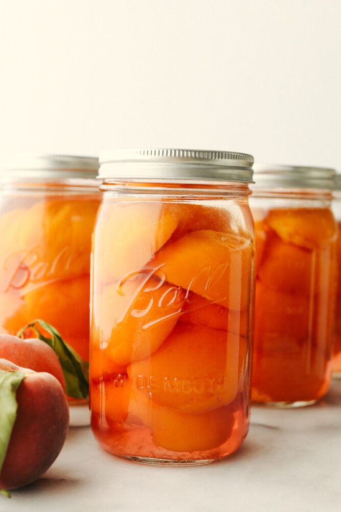 This in-depth guide to canning peaches gives you everything you need to know to have delicious peaches on hand year-round! It is easier than you would think and yields the sweetest, most delicious results each time. 3 jars of canned peaches.
