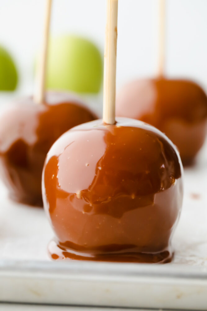 Celebrate fall by making these gourmet homemade caramel apples! They are the perfect blend of tart and sweet, topped with layers of indulgent caramel. 3 caramel apples on parchment paper.
