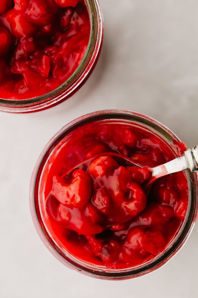 This cherry pie filling comes together so quickly and will make enough for you to have on hand for pies all year!! Delectable and sweet with a hint of tartness, this filling is perfection and you won't be able to go back to store-bought ever again!! Cherry pie filling in a jar with a spoon.