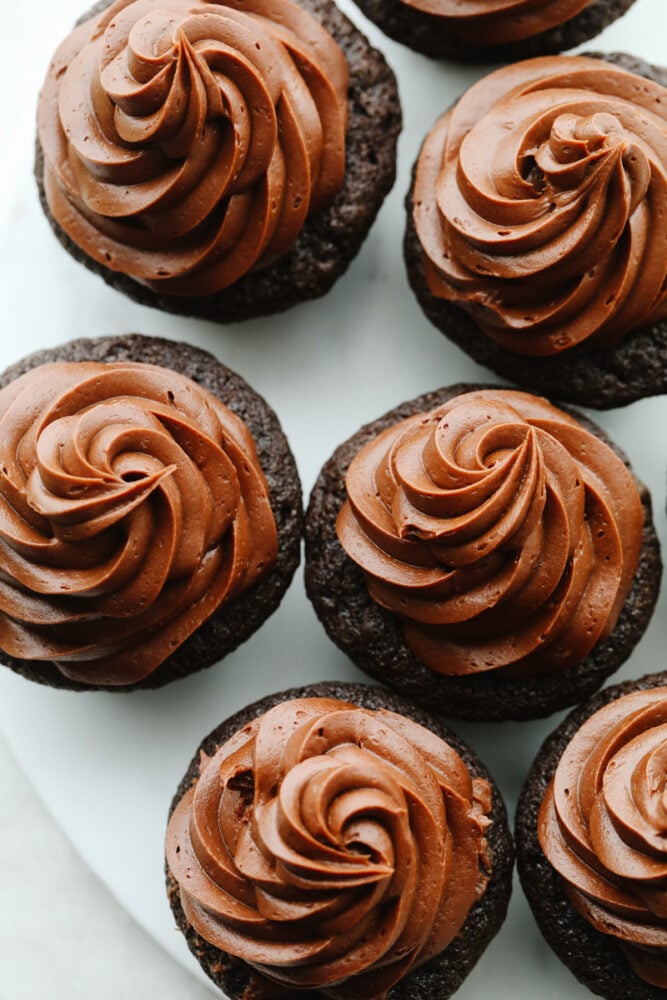 Chocolate buttercream frosting is creamy, smooth, rich, and mouthwatering! The chocolate flavor is absolutely incredible and you will want to add it to every single treat that you bake up this fall! Chocolate buttercream frosting on top of chocolate cupcakes.
