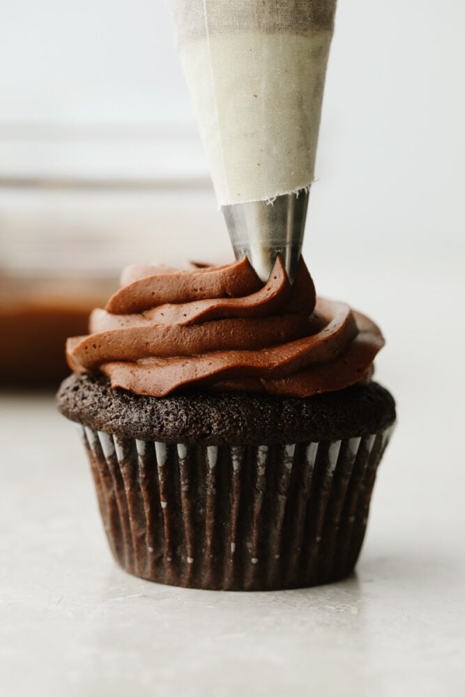 Chocolate buttercream frosting is creamy, smooth, rich, and mouthwatering! The chocolate flavor is absolutely incredible and you will want to add it to every single treat that you bake up this fall! Chocolate buttercream being piped onto a chocolate cupcake.