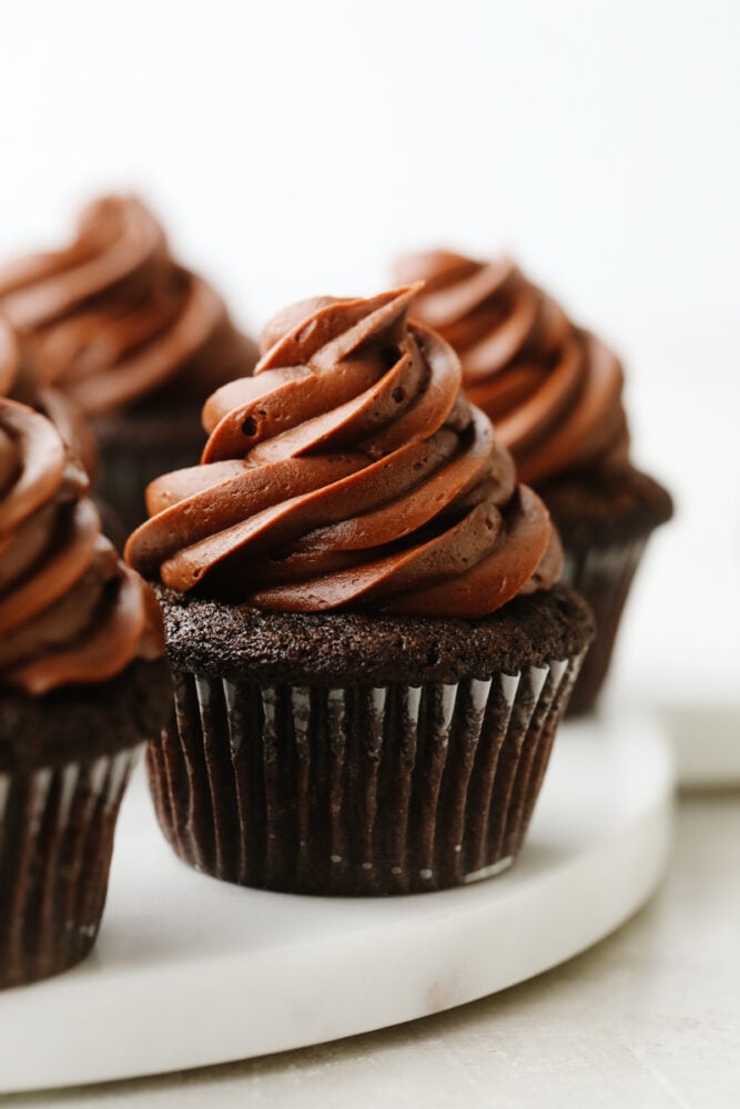 For treats that are incredibly moist, fudgy, and delicious, this is your go-to recipe! Topped with smooth chocolate buttercream, these chocolate cupcakes are a classic dessert your friends and family will go crazy over. Frosted chocolate cupcakes on a serving dish.