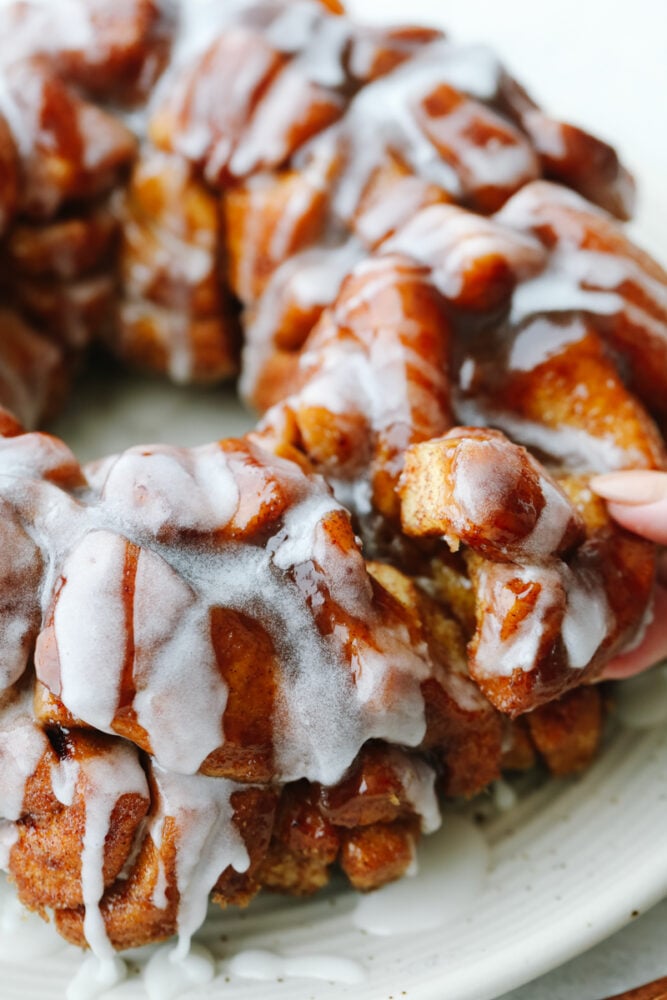 Cinnamon roll monkey bread is the easiest pull-apart dessert! It is amazingly soft, warm, and layered in decadent icing. Closeup of taking a piece of cinnamon roll monkey bread.
