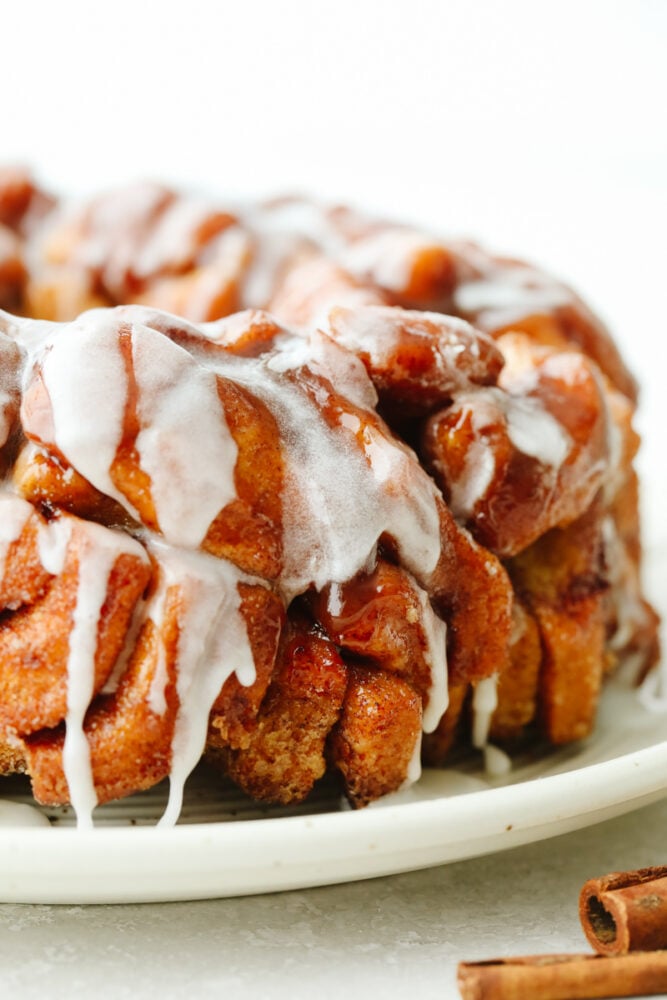 Cinnamon roll monkey bread is the easiest pull-apart dessert! It is amazingly soft, warm, and layered in decadent icing. Finished cinnamon roll monkey bread on a white serving dish.
