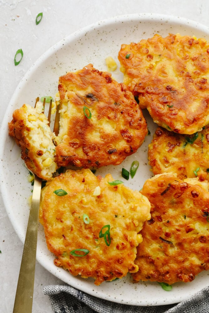 Corn Fritters are the best combination of savory tastes that are cooked to golden brown perfection! Crispy on the outside with a soft and tender inside, these are insanely delicious! Fritters on a plate being cut with a fork.