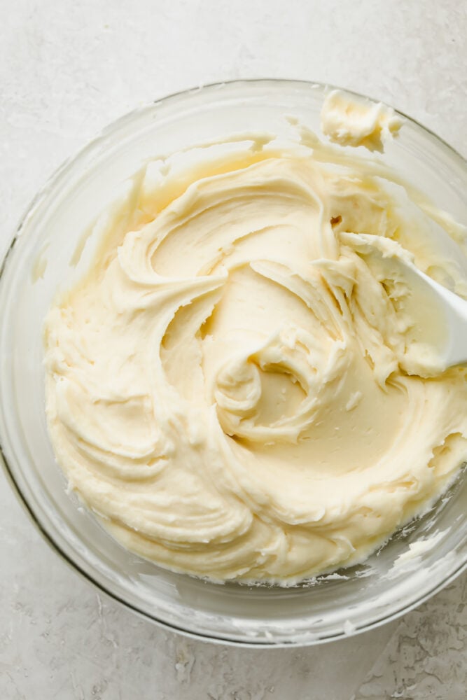 Cream cheese frosting that is insanely delicious and piped to perfection is exactly what this recipe is! It tastes amazing, looks beautiful AND it's super easy to make! Cream cheese frosting in a bowl with a spoon.