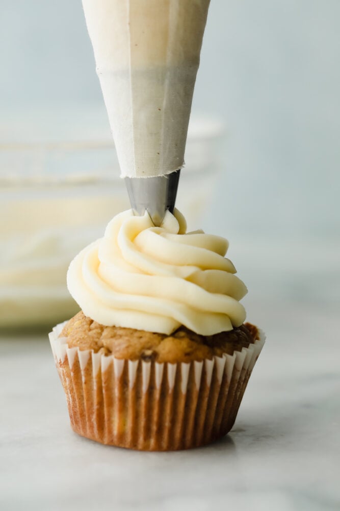 Cream cheese frosting that is insanely delicious and piped to perfection is exactly what this recipe is! It tastes amazing, looks beautiful AND it's super easy to make! Cream cheese frosting being piped onto a cupcake.