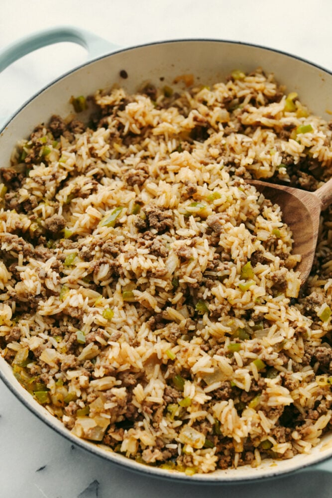 Why is it called โdirtyโ rice? The rice gets brown as it cooks with meat, Cajun spices, and the holy trinity of Cajun cooking: onion, bell pepper, and celery. My version combines ground pork and beef for a flavorful twist on this Louisiana classic! Dirty rice with meat and veggies being served with a wooden spoon.