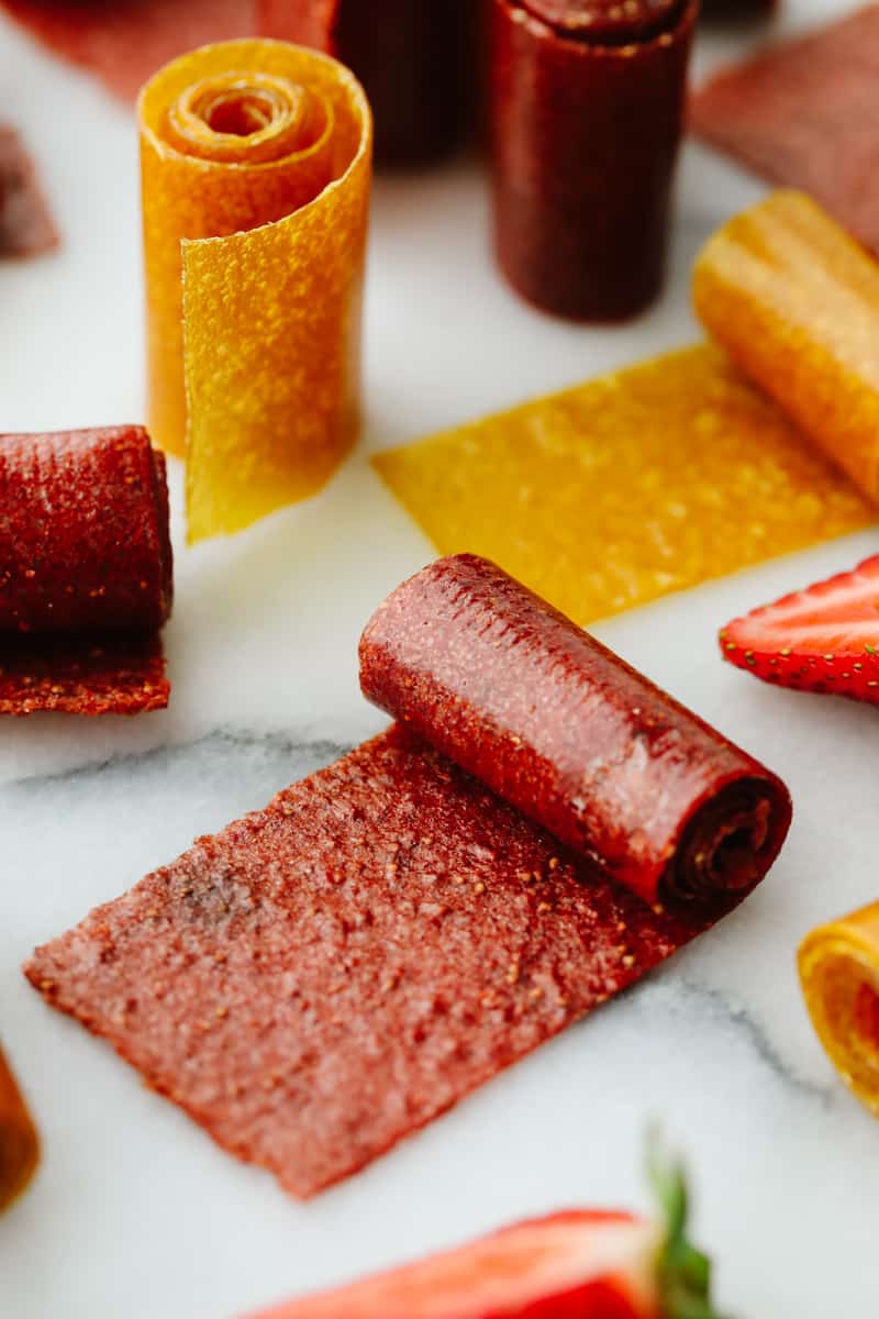 Homemade fruit leather is a fun, tasty way to turn ripe summer fruit into a snack that lasts all year! Just a few simple ingredients, no special tools, and a quick prep, then let the oven do the rest. Rolls of strawberry and mango fruit leather on the counter.
