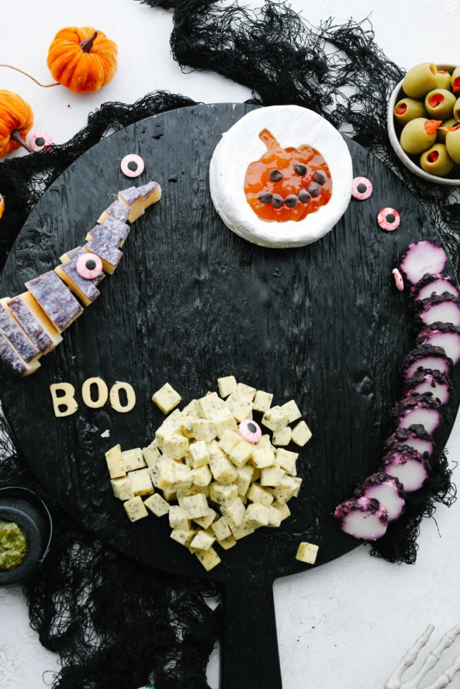This Halloween charcuterie board is a ghoulish treat for any party! A spooky twist on your classic cheese board, it's filled with fruit, crackers, and meat and sure to be everyone's favorite! Adding cheese to a board.