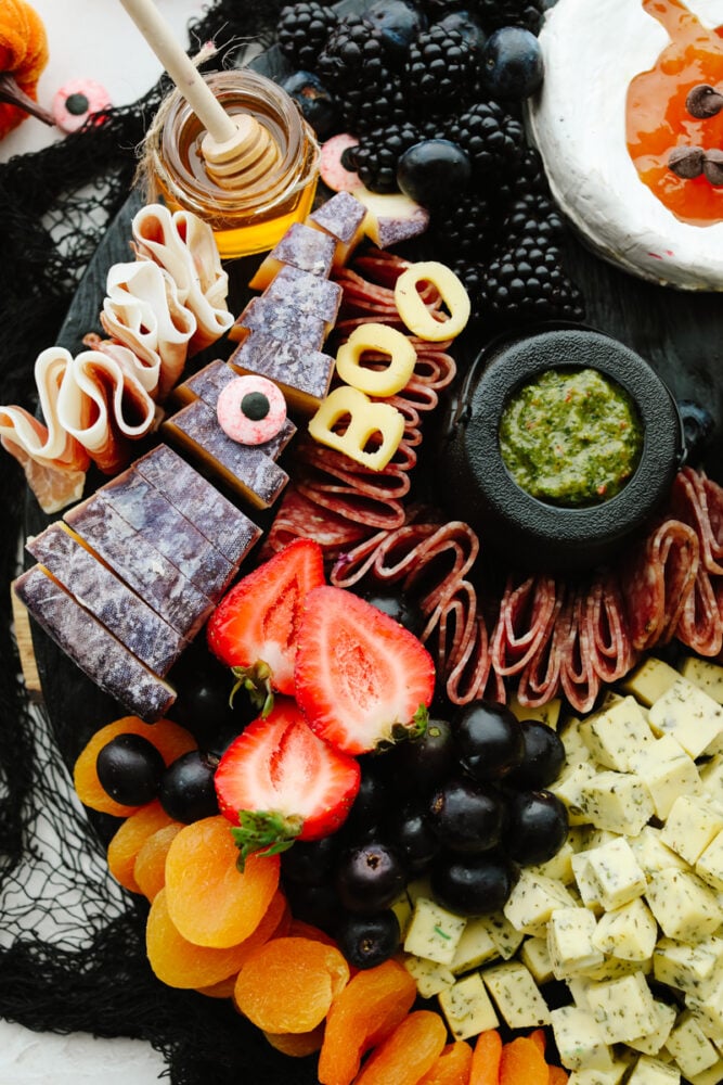 This Halloween charcuterie board is a ghoulish treat for any party! A spooky twist on your classic cheese board, it's filled with fruit, crackers, and meat and sure to be everyone's favorite! A charcuterie board with fruit being added.