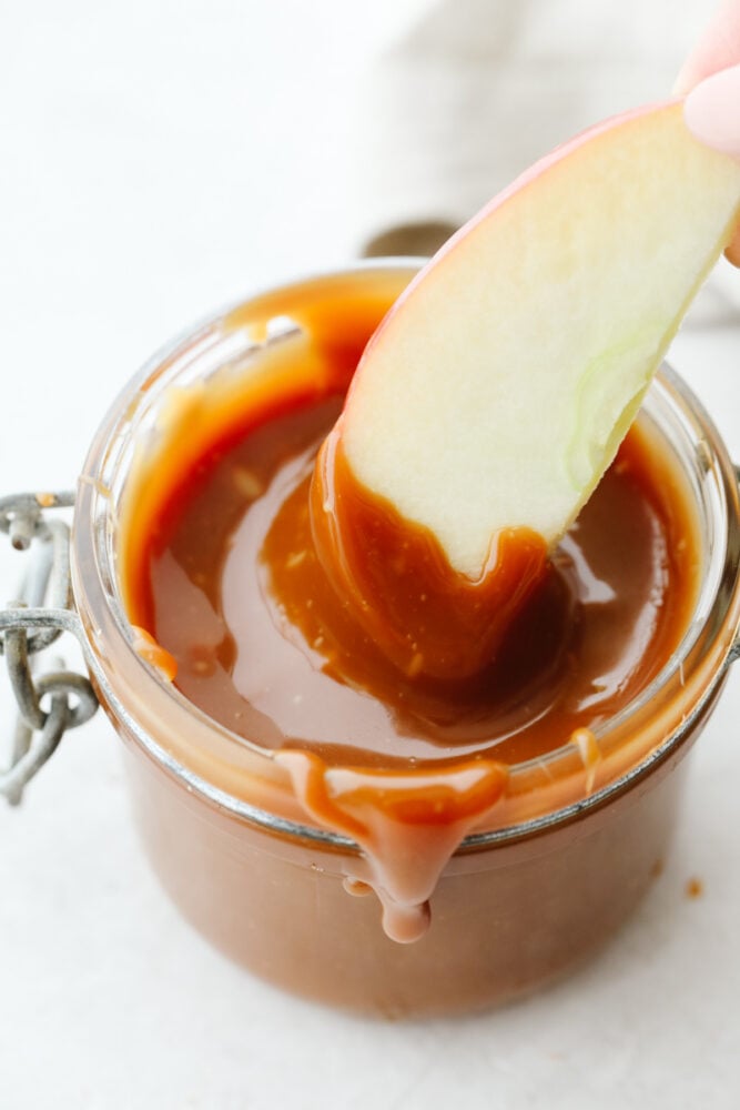 This homemade caramel sauce is straight from heaven! Its ooey-gooey, deliciously sweet flavor will have you over the moon excited, especially when you realize that you can add this to just about anything! An apple being dipped in caramel sauce.