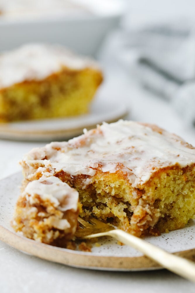Honeybun cake is a super moist cake swirled with cinnamon and sugar and covered in a delicious vanilla glaze. Absolutely mouthwatering, this tried and true recipe tastes like a cinnamon roll but in cake form! Honeybun cake being cut with a fork.